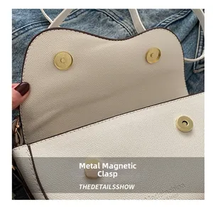 Dettaglio della borsa a sella in pelle bianca con chiusura magnetica in metallo oro