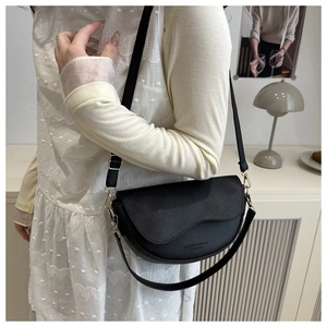 Dettaglio di una borsa a sella nera in pelle martellata con tracolla regolabile e parti metalliche