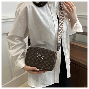 Brown monogram camera bag with a metal bow accent and striped woven shoulder strap