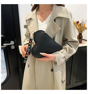 Detail of a heart-shaped black leather handbag with a LOVE wrist strap on a trench coat