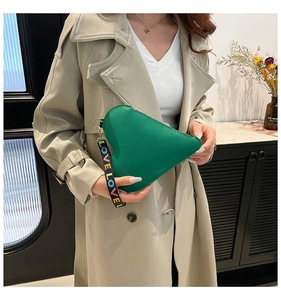 Detail of green heart-shaped leather clutch with colorful LOVE strap on beige coat