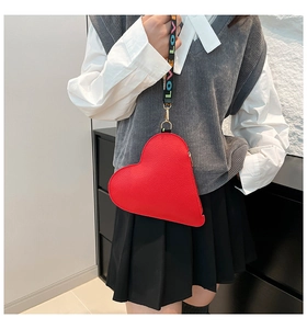 Detail of red heart-shaped bag featuring wide LOVE lettered woven shoulder strap