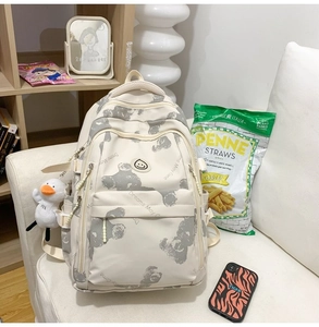 Detail of cream backpack with bear print and cute white duck plush keychain accessory