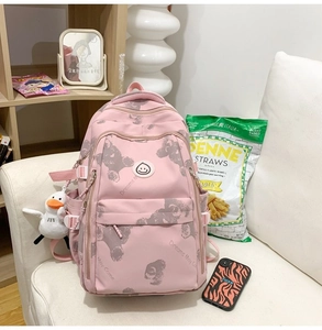 Pink nylon backpack with cute bear print and plush duck charm on a white fabric sofa