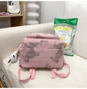 Detailed view of pink backpack with bear prints and a white plush charm on a sofa