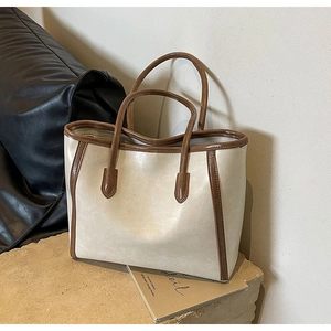 Detail view of large cream tote bag with brown handles on a stone background