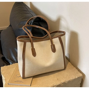 Detail of a large tote bag with cream leather body and brown trim on stone base