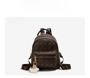 Front view of a dark brown mini backpack with bear patterns and a plush white pendant