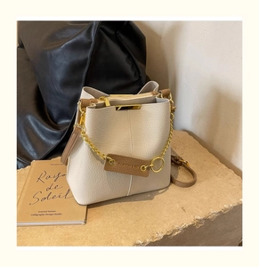 Detailed macro view of cream-colored pebble leather bucket bag with gold chain and tag