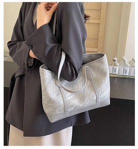 Detail shot of light grey tote bag with pleated texture held by a model in a minimal setting