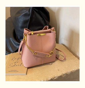 Detail of pink lychee textured leather bucket bag with gold chain and hardware accents