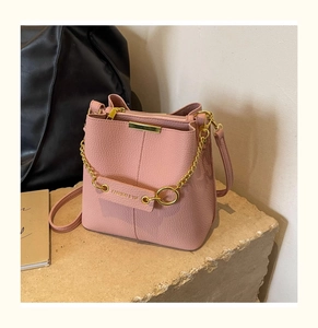 Detailed view of pink pebble leather bucket bag with gold chain and logo tag on stone surface