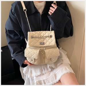 Detail of beige quilted backpack with metal chain straps and front pockets on dark jacket