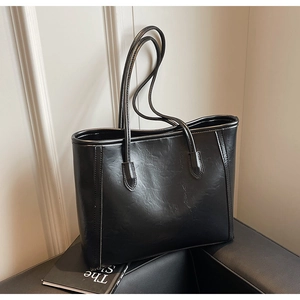 Detail of black tote bag featuring glossy pleated leather texture and slim shoulder straps