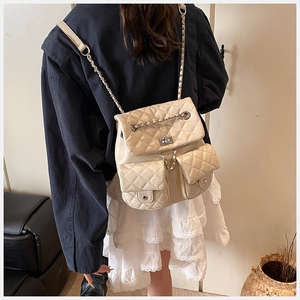 Quilted cream backpack with metal chain straps worn by model in a cozy home setting
