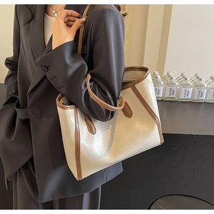 Detail of a large cream tote bag with brown leather straps worn over a grey blazer