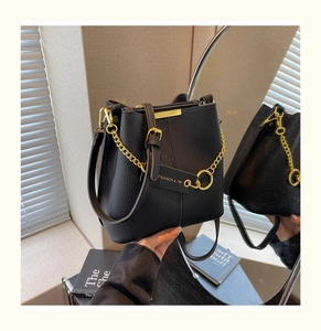 Detail of black lychee grain leather bucket bag with gold chain and fashion tag