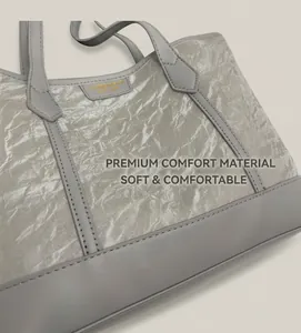 Close-up of grey pleated tote bag featuring golden metal brand logo and premium texture