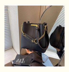 Detail of black lychee grain leather bucket bag with gold chain and metal logo bar