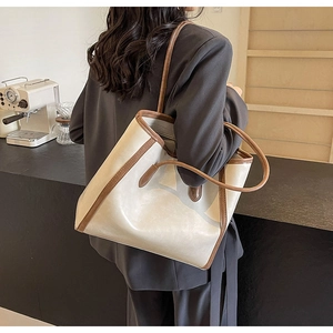 Detail of a large beige and brown tote bag carried by a model in a cozy cafe setting