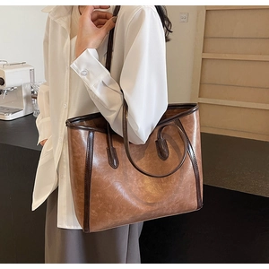 Brown vintage faux leather tote bag with contrast trim carried by a model in a cafe