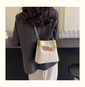 Detail of cream bucket bag in lychee leather worn with brown strap and gold chain