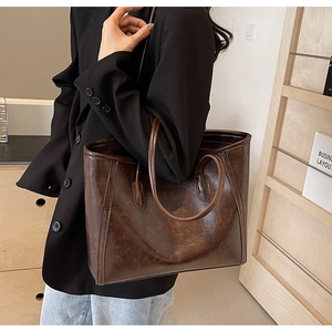 Detail of dark brown tote bag in oily faux leather finish worn on shoulder for commute