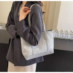 Detail of grey textured tote bag with smooth leather trim worn with grey blazer
