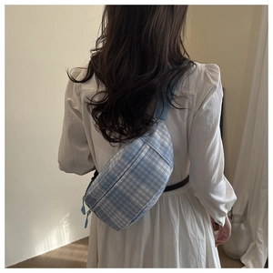 Detailansicht der hellblau karierten Bauchtasche am Modell vor einer neutralen Wand