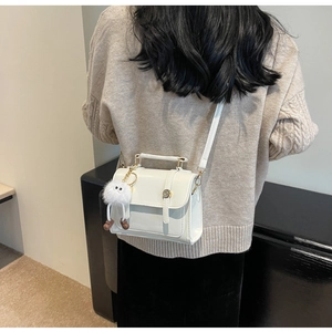 Detailweergave van een witte PU mini crossbodytas met een schattige pluchen pop hanger
