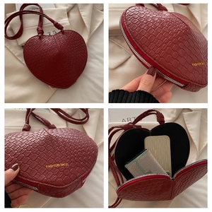 Detail view of heart-shaped red crossbody bag with crocodile texture and gold lettering