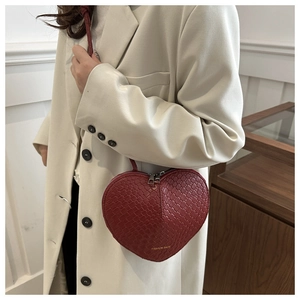 Detail of red heart-shaped woven texture crossbody bag with double zipper on model