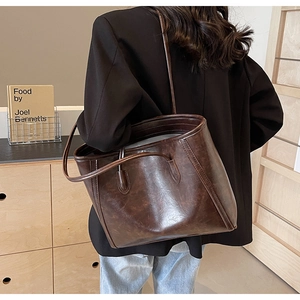 Detail of a large vintage brown faux leather tote bag worn by a model in a casual setting