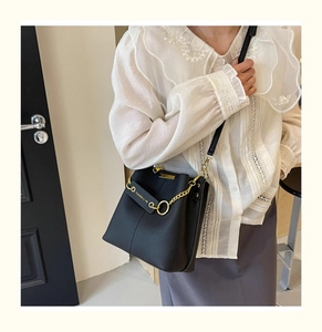 Close-up of black lychee leather bucket bag with gold chain strap on lace top