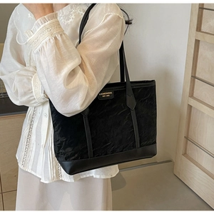 Detail of black pleated tote bag with gold metal logo and leather base on white shirt