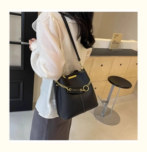 Detailed side view of black pebbled leather bucket bag with gold chain and leather strap