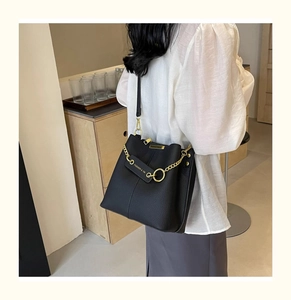 Detail of black lychee grain leather bucket bag with gold chain and metal logo plate