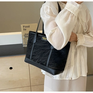 Detail of black pleated tote bag showing fabric texture and faux leather strap on model