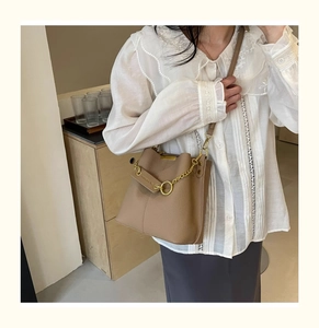 Detail of brown litchi pattern bucket bag with golden chain and ring hardware on model
