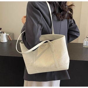 Detail of white leather tote bag featuring natural pleated texture and logo lettering