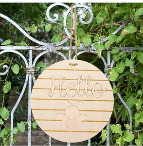 Close-up of a round wooden door sign featuring a 3D Hello text and bee pattern detail
