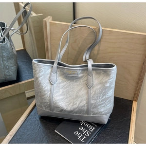 Close-up of silver-grey tote bag showing textured pleats and golden brand logo plaque