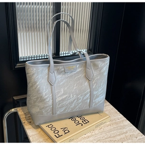 Detail of silver gray pleated tote bag with golden logo on marble surface and books