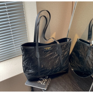Detail of black wrinkled tote bag featuring a metallic logo plate and slim shoulder straps