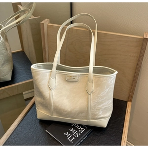 Close-up of creamy white tote bag featuring unique crinkled texture and metal logo plate
