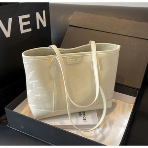 Close-up of pleated cream tote bag with gold brand plate in luxury gift box