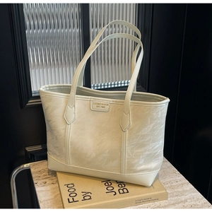 Close-up of cream-white tote bag featuring marble-textured leather and gold brand plate