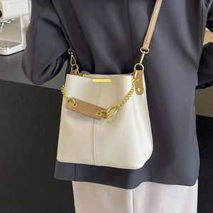 Fashionable creamy white leather bucket bag with gold chain strap shown on a person