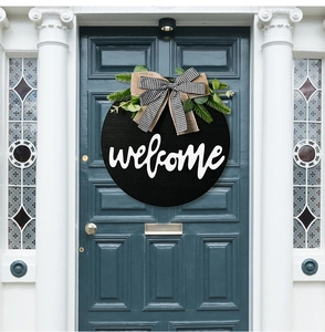 Detail of round black wooden welcome sign with jute bow and eucalyptus on a blue door