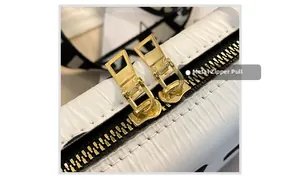 Detailed close-up of premium gold-toned metal zipper heads on a white shoulder bag